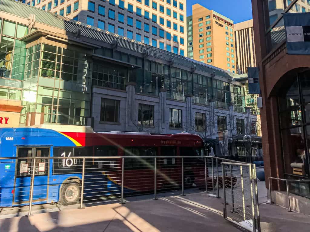 A red and blue bus is picking people up on the street in a city.