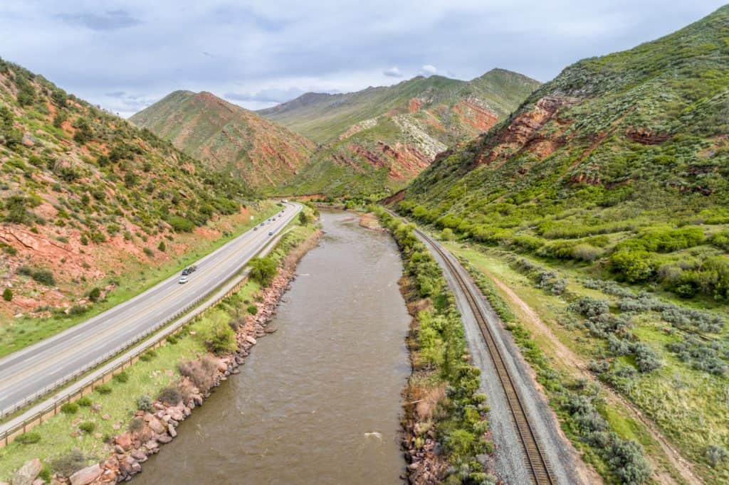 A river cutting through the mountains with a road on one side and train tracks on the other. 