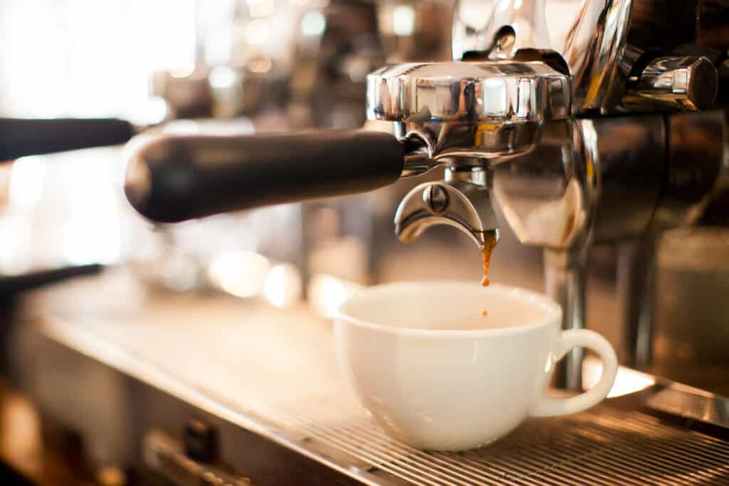 Espresso being extracted from a portafilter machine into a white ceramic cup, highlighting the golden brown coffee dripping with a blurred background.